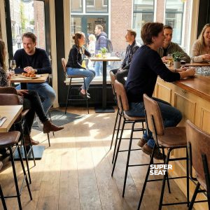 Super-Seat | Barkrukken in cognac leer and metaal bij houten tafels in café met bakstenen muren, veel licht. | Horecameubilair