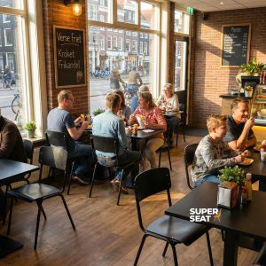 Super-Seat | Vanitas vintage schoolstoelen zwart in café Zwarte metalen stoelen, houten tafels ; grote ramen, licht en gezellig. | Horecameubilair