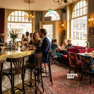 Super-Seat | Pub Interieur | Donkerbruine houten Thon barkrukken, fluwelen stoelen, tafels, grote ramen en patroonkleed in warme sfeer. | Horecameubilair