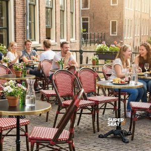 Les chaises empilables en osier et les tables de patio en bois de Super-Seat sont installées à l'extérieur, le long de la rue des enfants. | Mobilier de restauration