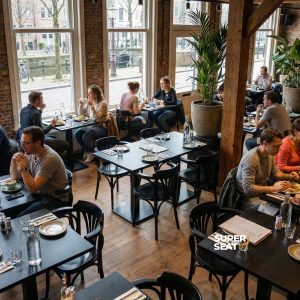 Chaises et tables en bois noir, plantes vertes, sol en bois et murs en briques. | Mobilier de restauration