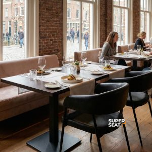 Super-Seat | Chaises Maxwell noires en tissu et métal, tables en bois, mur en briques dans un restaurant ensoleillé. | Mobilier de restauration