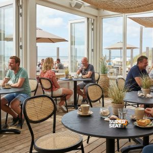 Super-Seat | Chaises et tabourets de bar noirs autour de tables en HPL noir rouille/cuivre, vue sur les dunes et la mer. | Mobilier de restauration