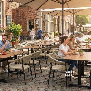 Super-Seat | Vous voyez des tables de terrasse en teck, des chaises en métal, des bacs à fleurs et de grands parasols dans une rue pavée. | Mobilier de restauration