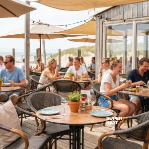 Super-Seat |Tables rondes en bois teck 70cm, chaises en métal noir, parasols, dunes de sable en arrière-plan. | Mobilier de restauration
