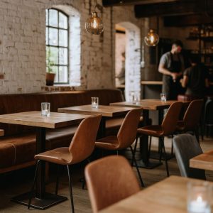 Super-Seat | Intérieur d'un restaurant moderne avec tables en bois | Houten tafels, vintage cognac leren stoelen, bruine stoffen bank, witte bakstenen wanden |. | Horecameubilair