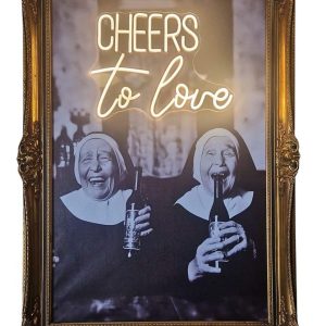 Super-Seat | Une photo en noir et blanc de religieuses avec l'art "CHEERS" en néon dans un cadre orné en bois doré | Zwart-wit kunstwerk in sierlijke gouden lijst, materiaal hout & neon, kleur zwart-wit/goud/neon. | Horecameubilair