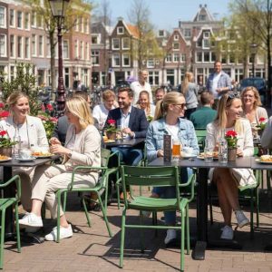 Super-Seat | Tables en HPL noir, chaises en métal, personnes mangeant à l'extérieur parmi les fleurs et les vélos. | Mobilier de restauration