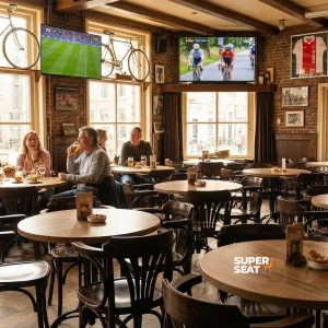 Super-Seat |Tables, chaises et tabourets de bar en bois ; couleur chêne chaud dans un bar sportif avec des vélos au mur. | Mobilier de restauration