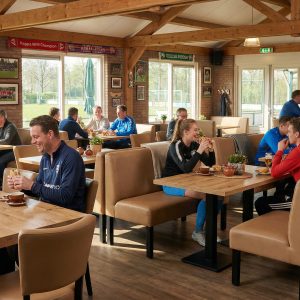 Super-Seat | Lisa hospitality dining bench bistro Taupe - 120cm | Banc de salle à manger Taupe avec table en bois, chaises en métal dans un café lumineux avec décor sportif et poutres en bois. | Mobilier de restauration