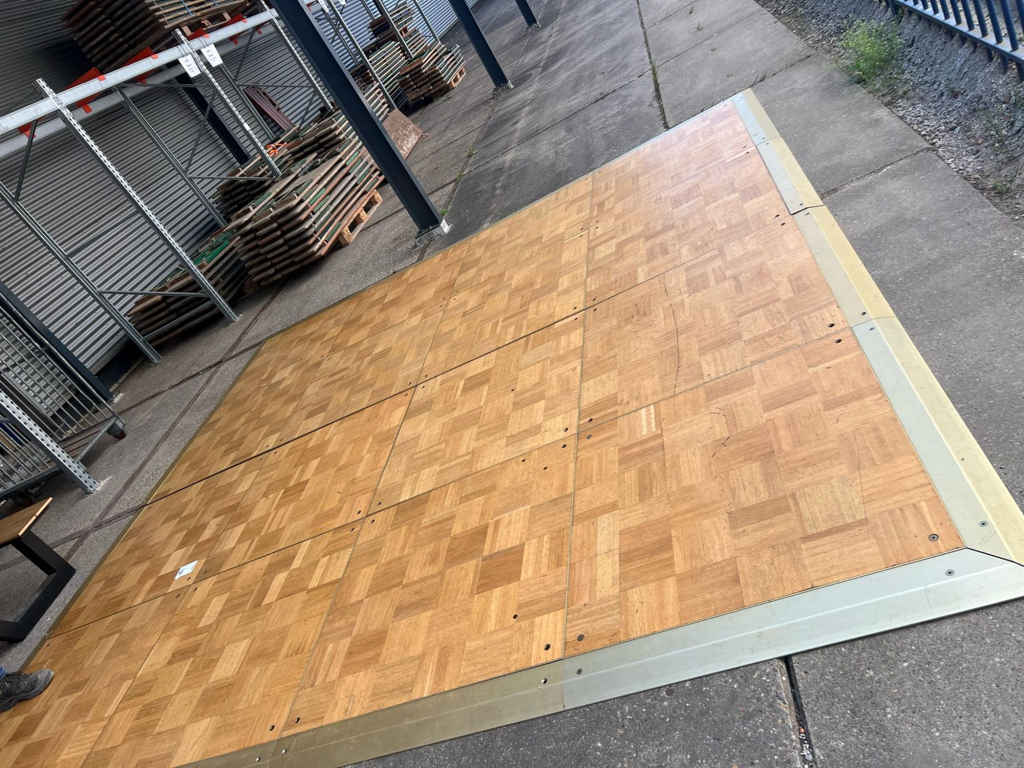 Super-Seat | Piste de danse mobile, plancher en bois avec bord en laiton d'environ 15m2 | Piste de danse en bois brun avec bord en laiton doré, placée sur du béton à l'extérieur. | Mobilier de restauration