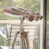Super-Seat | Jumelles chromées argentées sur trépied en bois ; à l'arrière-plan, une chaise en bois, vert à l'extérieur. | Mobilier pour la restauration