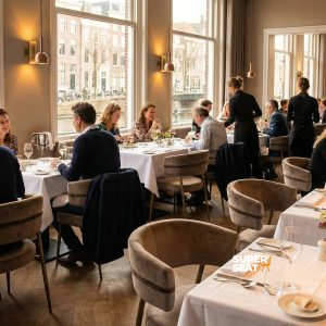 Super-Seat | Mounira Design Fauteuils en velours moka avec détails dorés, tables blanches et arrangements floraux dans un restaurant au bord de l'eau. | Mobilier de restauration