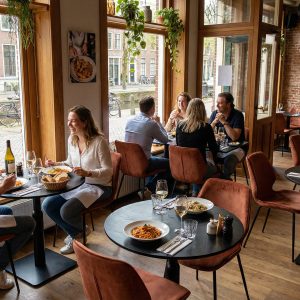 Super-Seat | Zwarte metalen tafels, houten stoelen en barkrukken in restaurant met bakstenen muren. | Horecameubilair